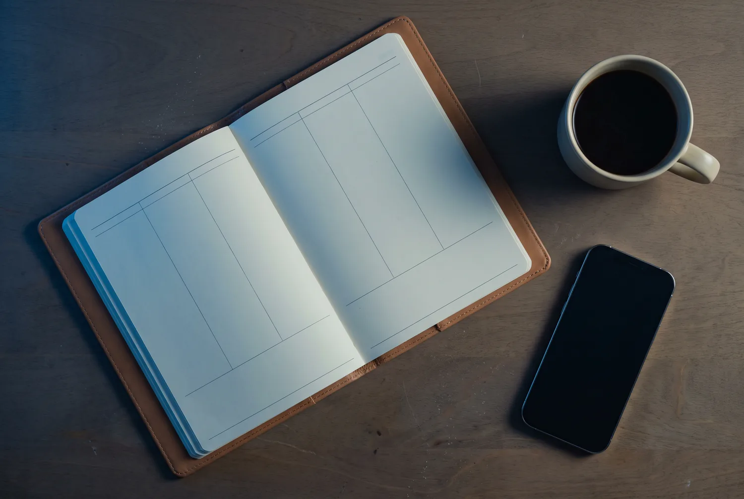 The same planner at dusk with both pages empty, phone face down, coffee gone cold